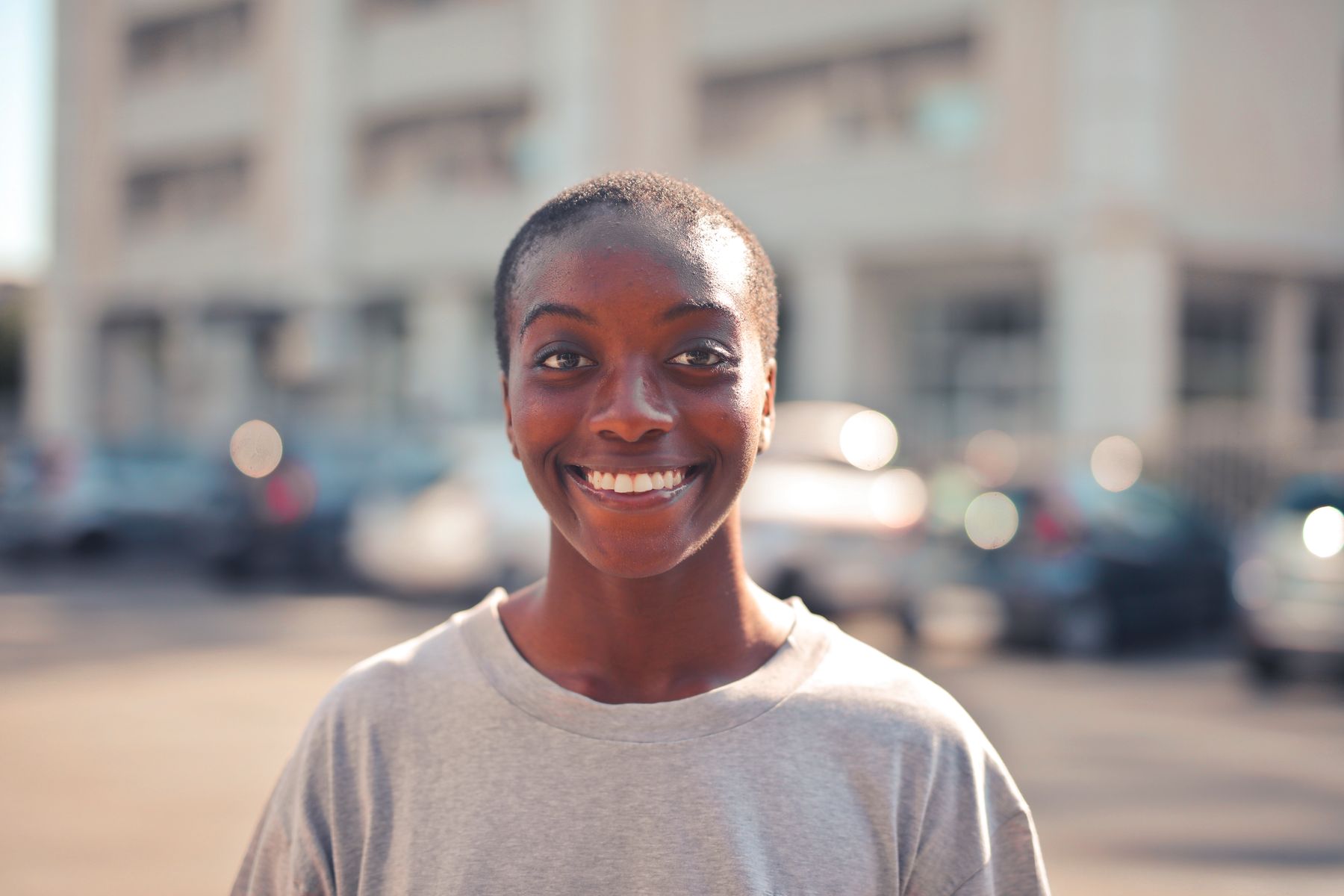 A woman smiling on a sunlit street, photograph by Andrea Piacquadio on Pexels