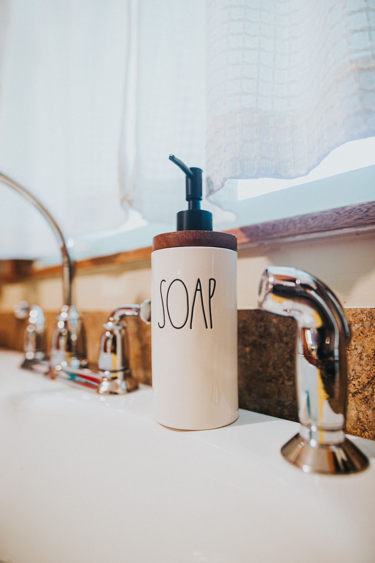 White ceramic soap dispenser with a timber lid on a bathroom basin