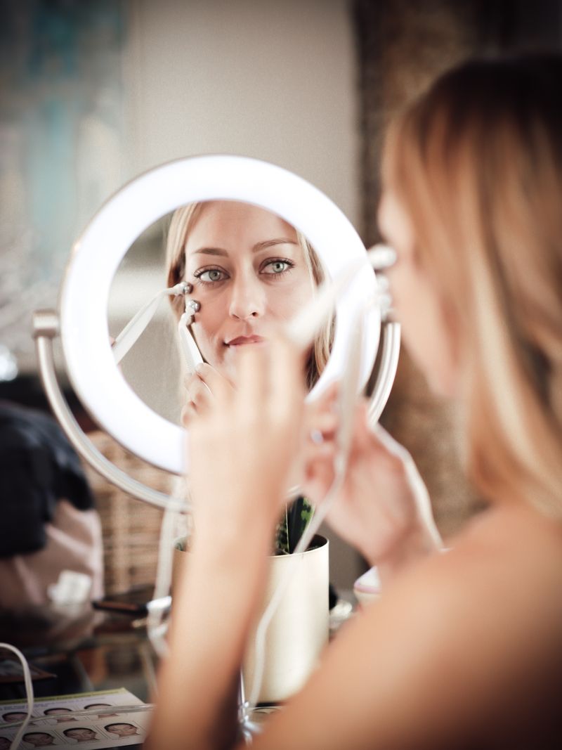 Woman using a handheld facial device in front of a mirror