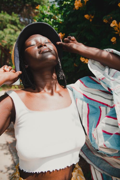Free A woman in a white tank top enjoys the sunlight with eyes closed outdoors. Stock Photo