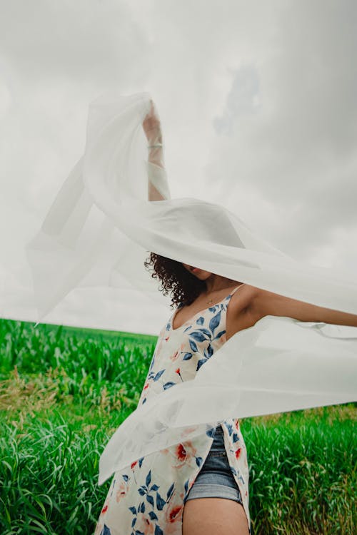 Woman in White and Blue Floral Dress Lying on Green Grass Field