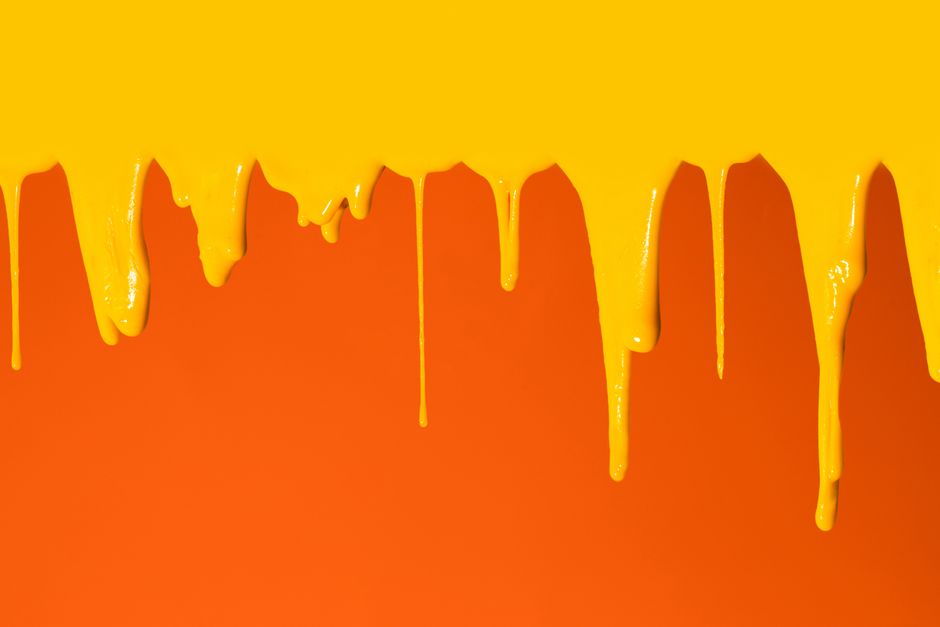 Abstract image of vivid yellow paint drips against an orange backdrop.