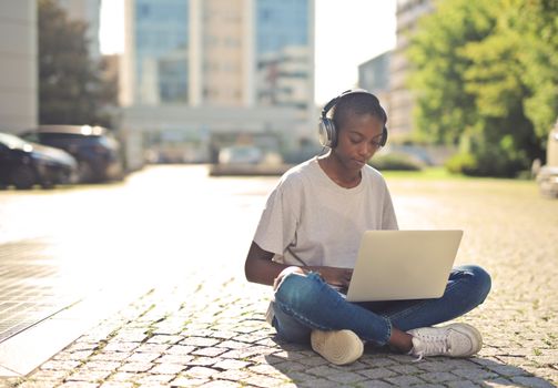 Young woman sitting outdoors, using a laptop for online learning on a sunny day.