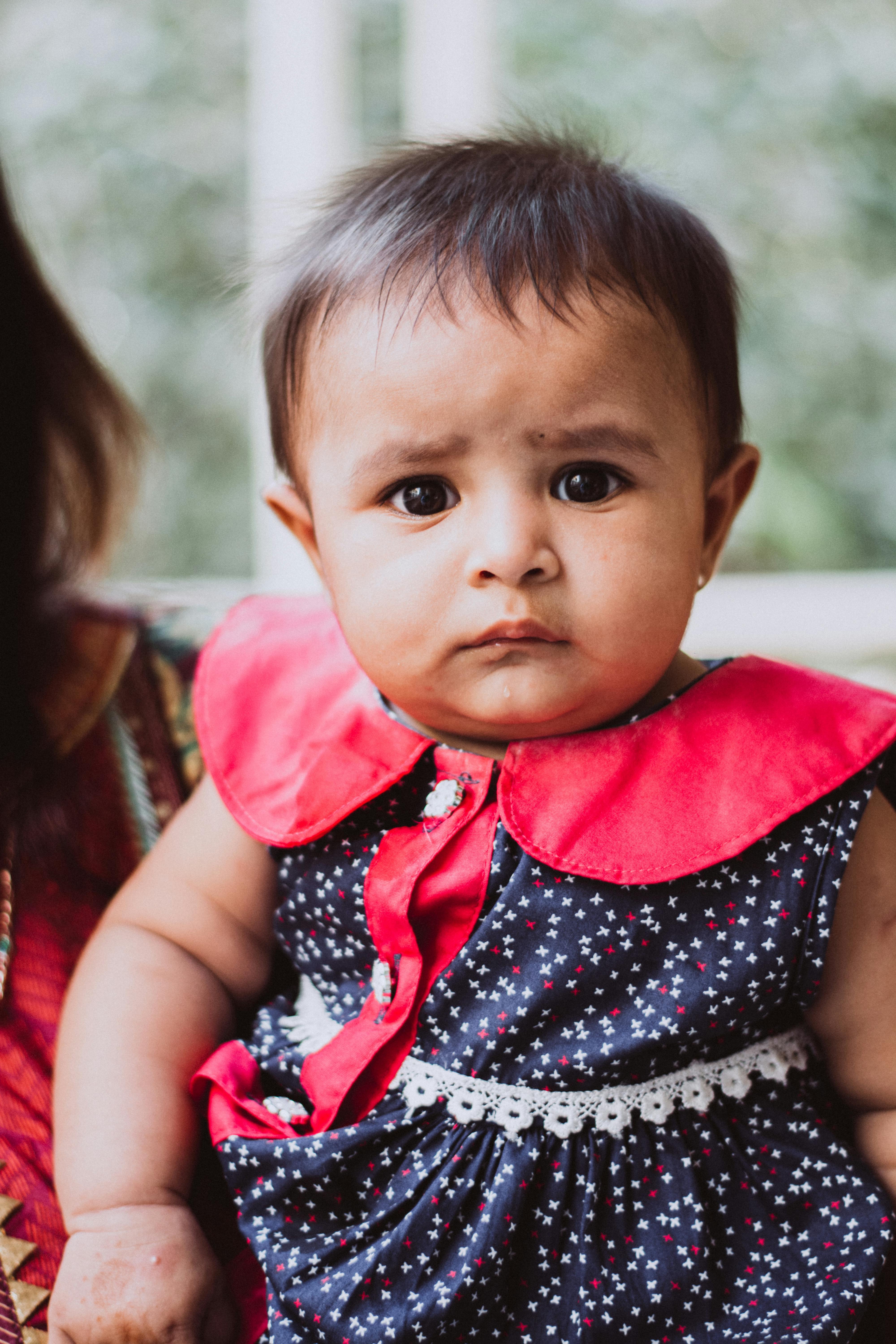 室内，一个穿着鲜艳连衣裙的婴儿表情严肃地拍着照片