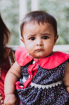 室内，一个穿着鲜艳连衣裙的婴儿表情严肃地拍着照片