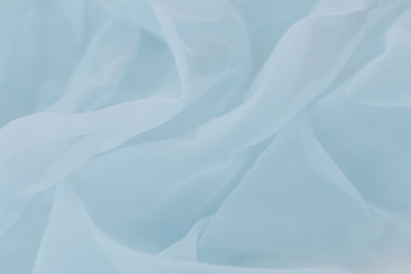 Close-up of a thin pale blue cloth in soft ripples, light passing through the layers.