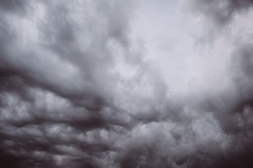 From below black and white view of dramatic overcast skies with dense cumulus clouds in haze