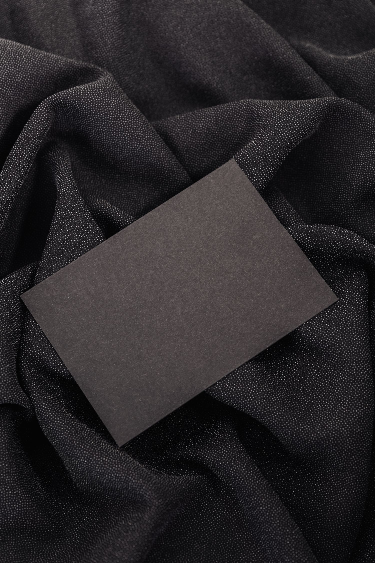 Black card on textured black fabric background, ideal for mockups and design presentations.