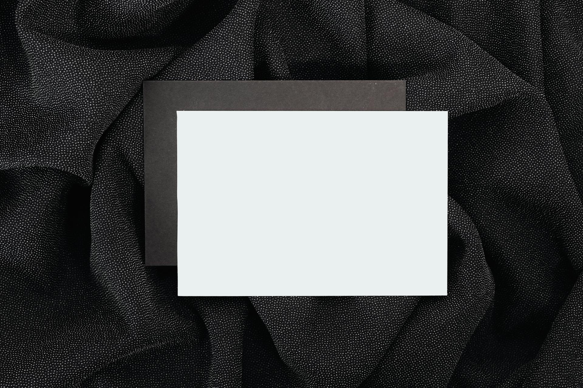 Blank black and white card on textured black cloth, ideal for designs.