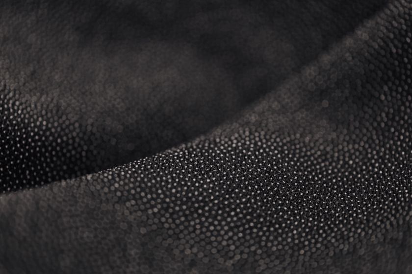 Macro close-up of a black cloth covered in small regular dot motifs that follow the curve of the fold.