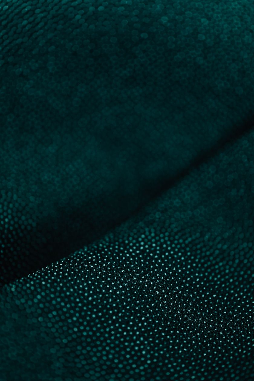 Close-up of a dark teal technical knit, a fine even dotted face curving smoothly through one fold.
