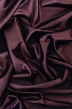 特写镜头捕捉起皱的闪亮紫色缎面，凸显其光滑质地与窗帘的优雅