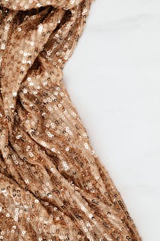 Close-up of gold sequined fabric, showcasing intricate texture and elegant shimmer against a white background.