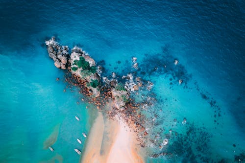 Picturesque drone view of yachts sailing near rocky formations and stones in tropical turquoise ocean with sandy beach