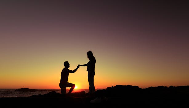 Silhouette of a couple's romantic proposal by the beach during a stunning sunset.