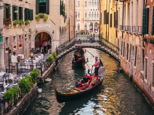 Free Charming scene of gondolas navigating a canal in Venice, Italy with a backdrop of historic buildings and a pedestrian bridge. Stock Photo