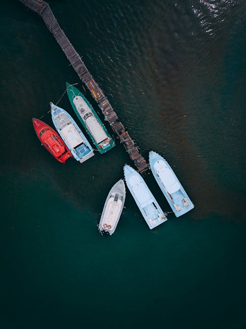 Aerial view of modern motorboats moored in sea near shabby wooden pier on sunny day