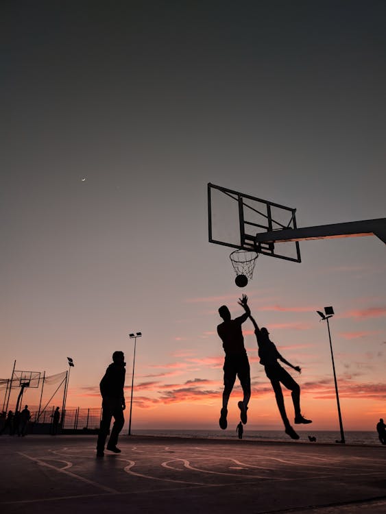 日没時にバスケットボールをする人々のシルエット