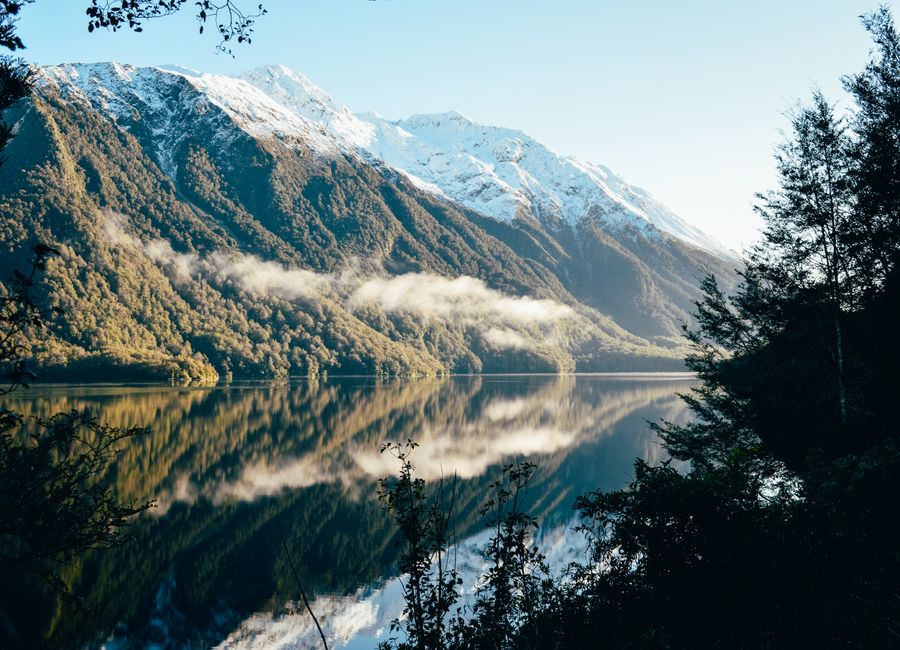 Breathtaking view of snow-capped mountains reflecting in a serene lake in Southland, New Zealand.