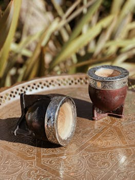 Two traditional yerba mate gourds on a rustic engraved tray in natural sunlight.