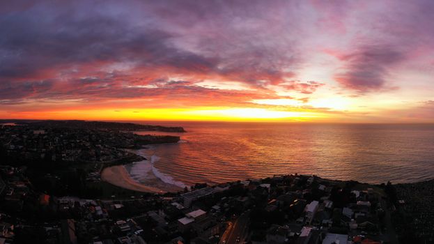 Stunning aerial view of a coastal city with vibrant sunset and dramatic skies over the ocean.