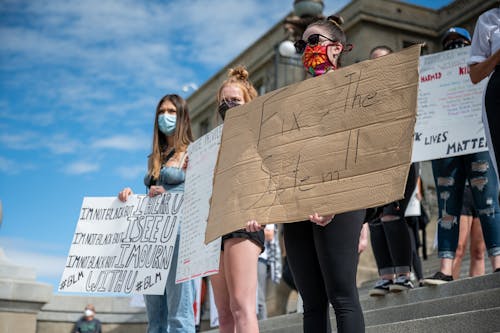 Free From below of unrecognizable protesters in face masks showing BLM placards on staircase in demonstration Stock Photo