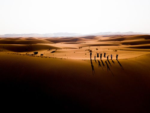 Free Aerial view of a group jumping in the Iranian desert at sunset with dramatic shadows and sand dunes. Stock Photo