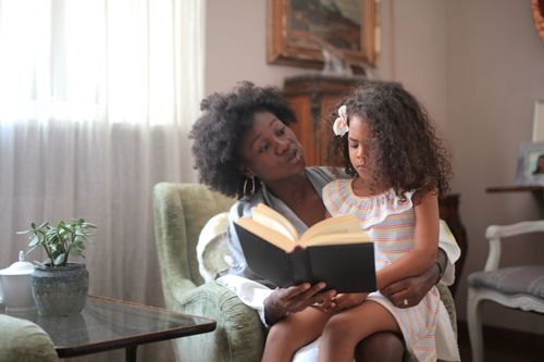 Free An African American mother reads a storybook to her daughter on a sofa, creating a warm bonding moment. Stock Photo