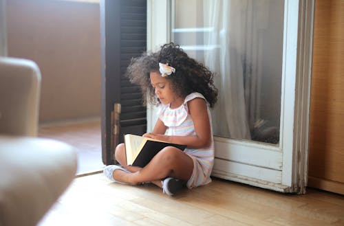 Girl Sitting on The Wooden Floor While Reading a Book