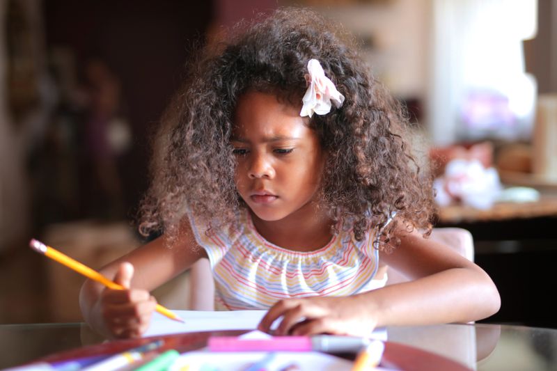 African American child focused on homework, writing with a pencil indoors.