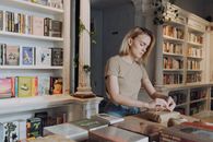 在一家温暖、迷人的书店里，一位年轻女子正在包装书籍，周围的书架上摆满了文学作品