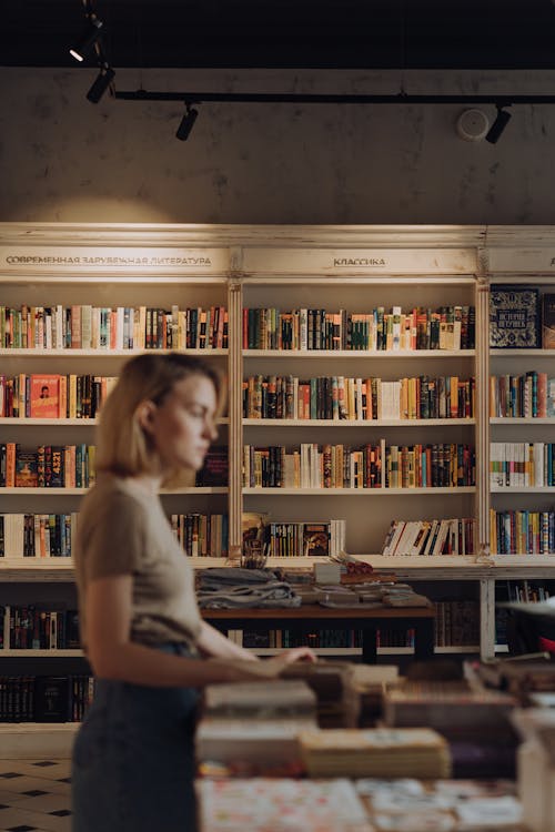 Woman in White Crew Neck T-shirt Standing in Front of Books