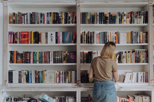 Free Blonde woman browsing a bookshelf in a library, conveying a love for reading and literature. Stock Photo