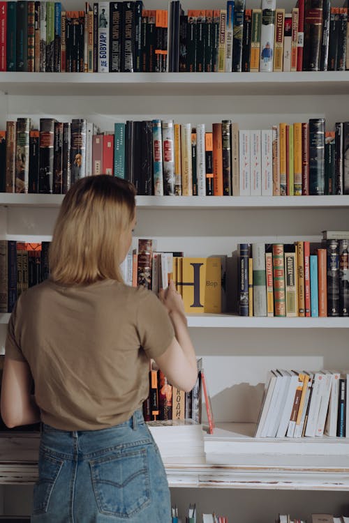 Женщина в коричневой футболке стоит перед книгами