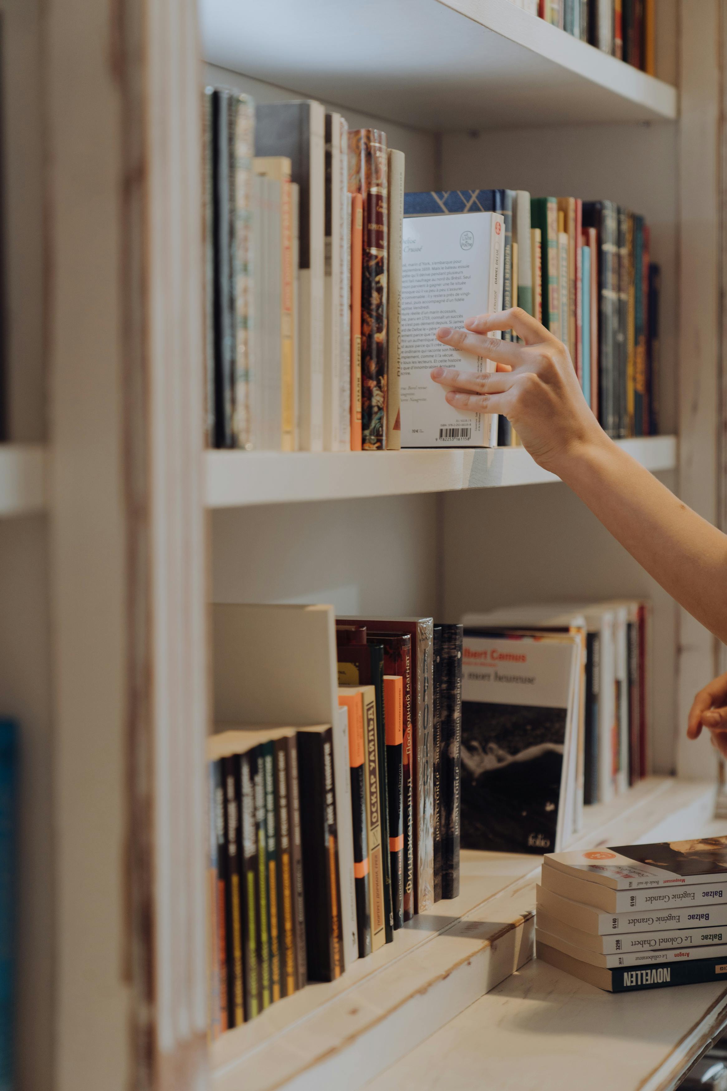 person holding white book in white wooden shelf