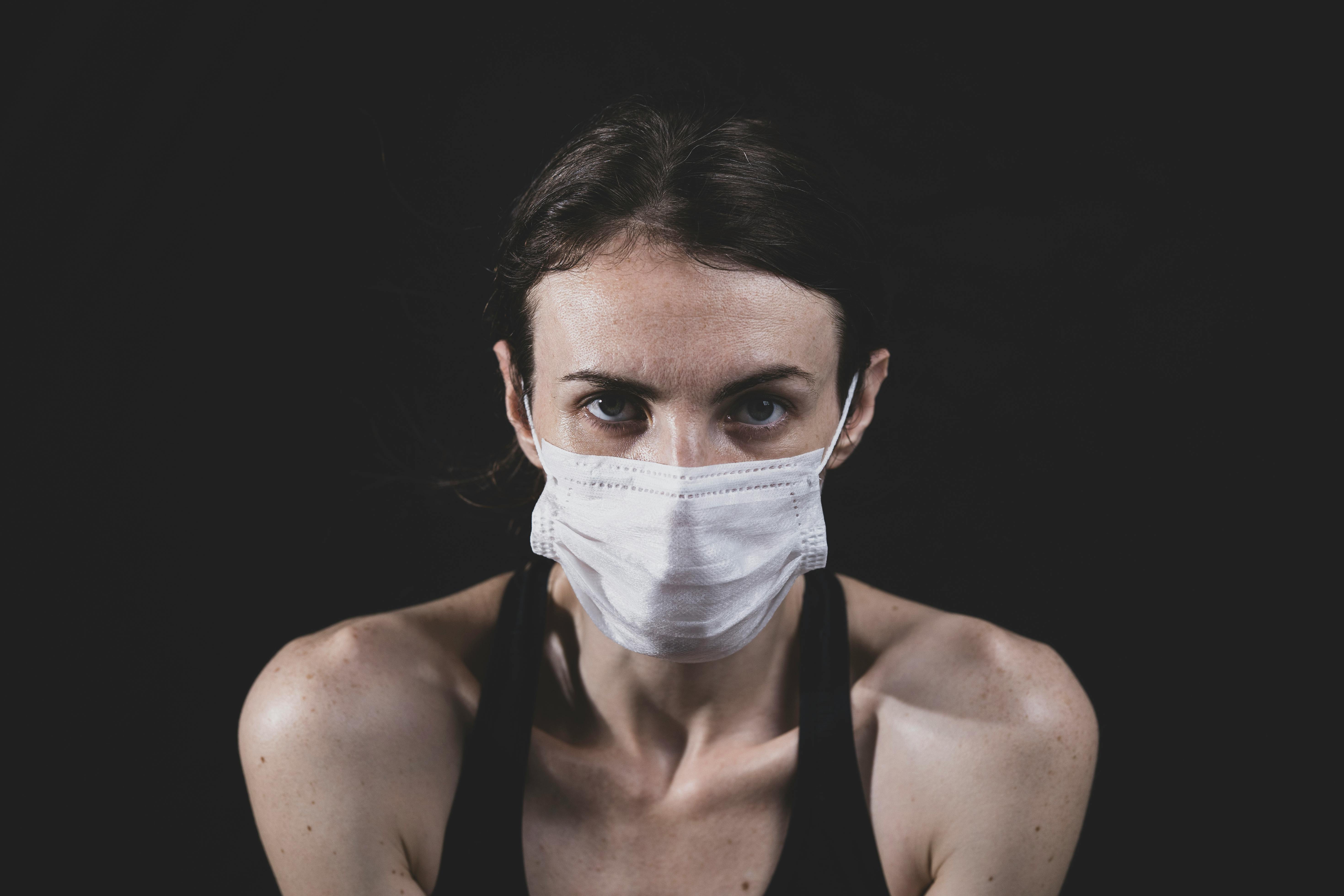 一名成年女性戴着口罩，在黑暗背景下的特写肖像，突出安全和健康