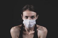 一名成年女性戴着口罩，在黑暗背景下的特写肖像，突出安全和健康