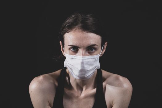 一名成年女性戴着口罩，在黑暗背景下的特写肖像，突出安全和健康