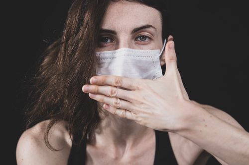 Free Close-up of a woman in a face mask covering her mouth with her hand against a black background. Stock Photo