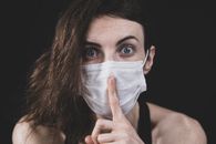 A woman in a face mask gestures for silence, emphasizing health precautions.