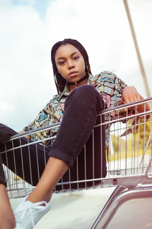 Free Trendy young woman with a serious look sitting in a shopping cart outdoors. Stock Photo