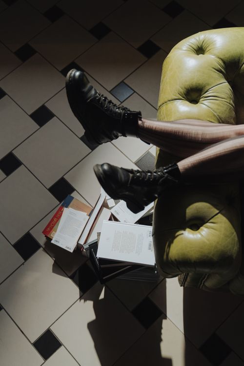Free A person lies on a sofa with boots, surrounded by books, enjoying leisure time. Stock Photo