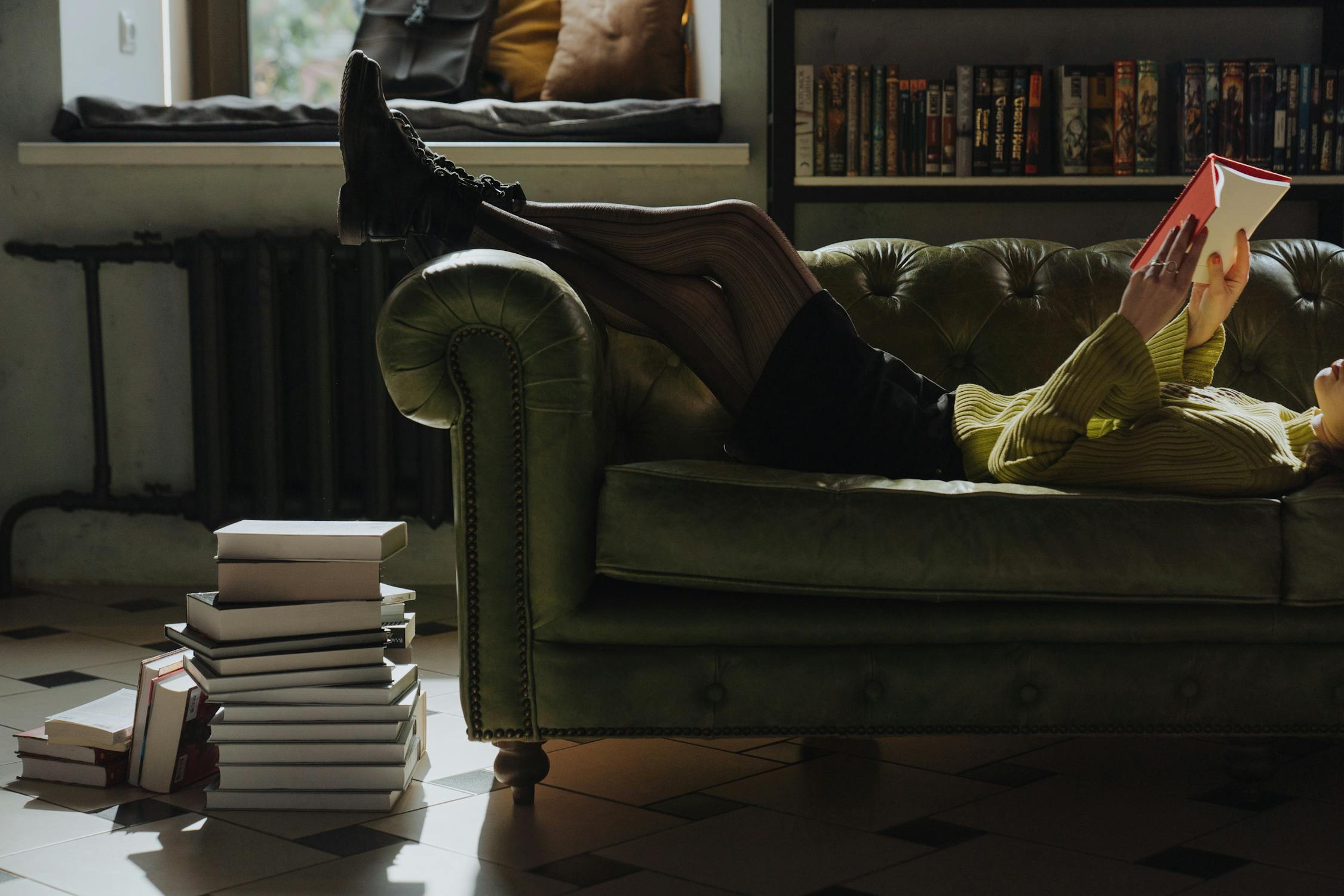 A young woman is reading a book on a sofa next to stacks of books. This reminds me of the most important spiritual books that help me to live with purpose.