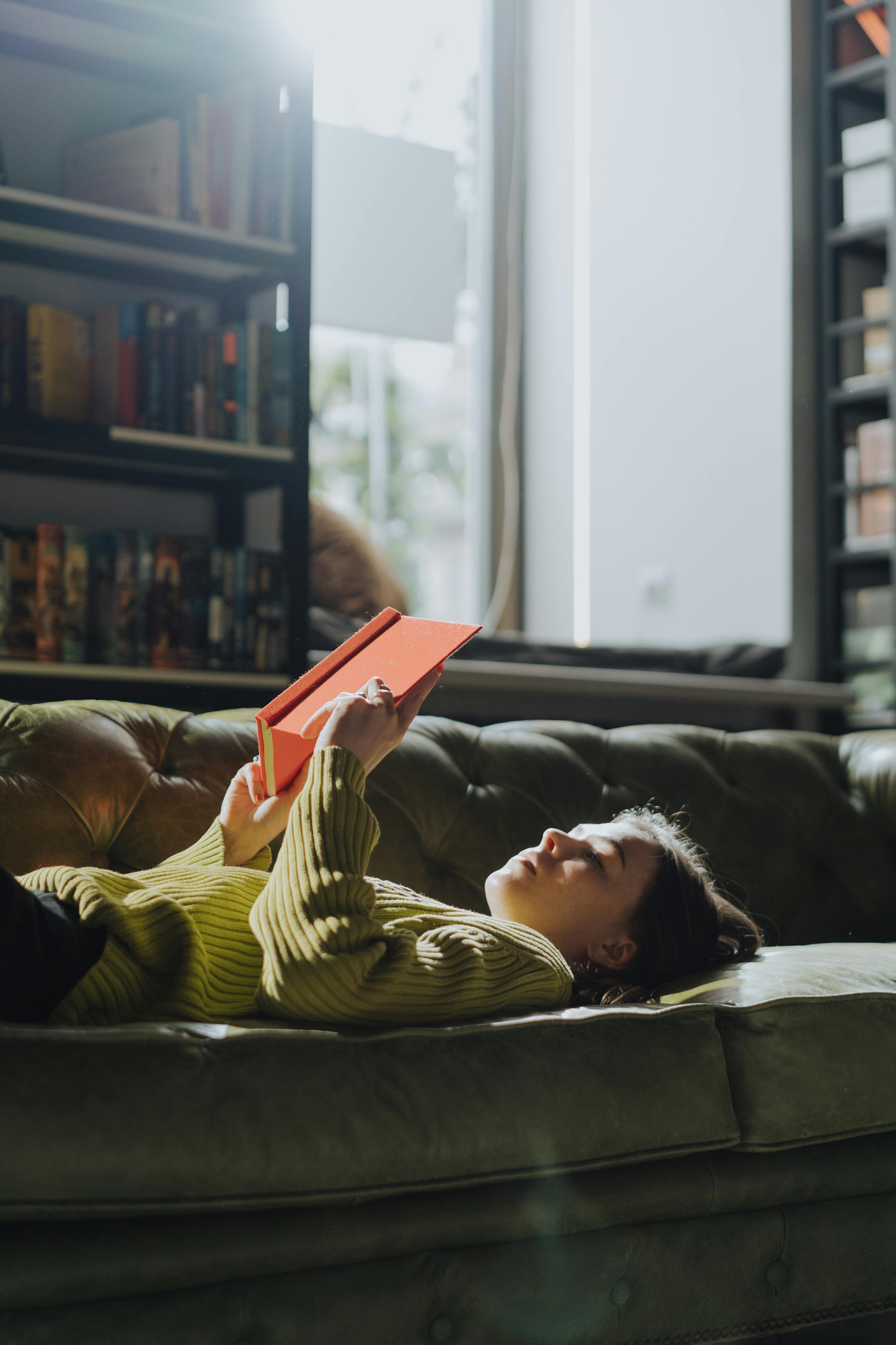 一位穿着绿色毛衣的年轻女子在室内沙发上放松地看书