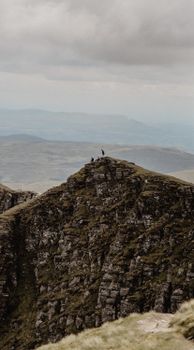 Hikers explore a remote mountain peak in Scotland under a dramatic cloudscape.