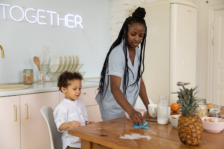 A Mother Wiping The Spilled Milk On The Wooden Table