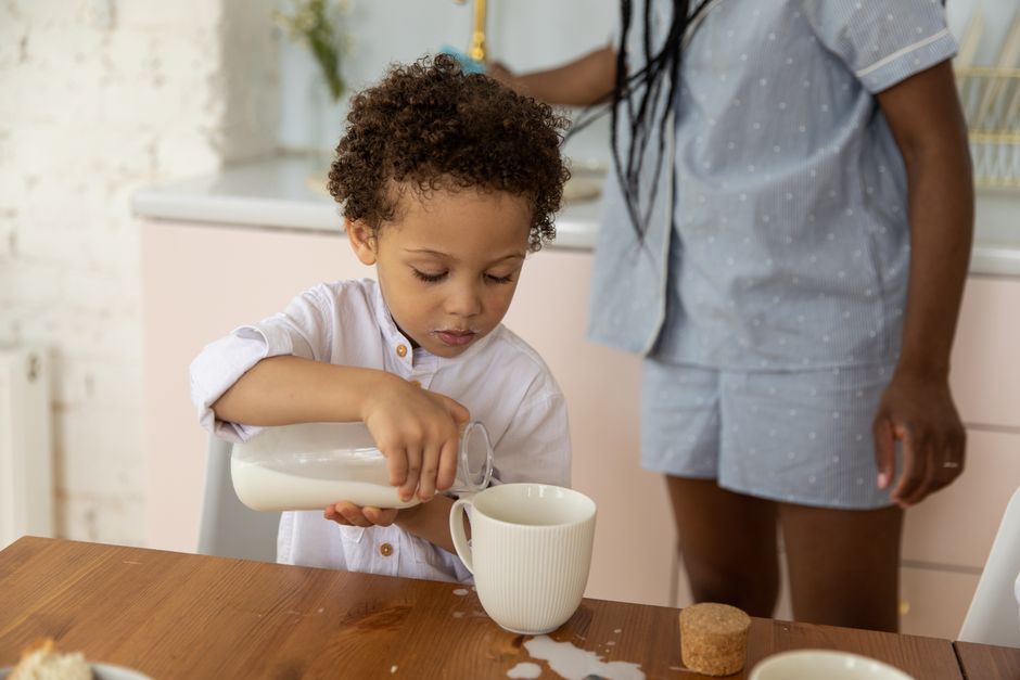 Ein Kind und ein Erwachsener genießen das Frühstück drinnen und gießen Milch in eine Tasse.