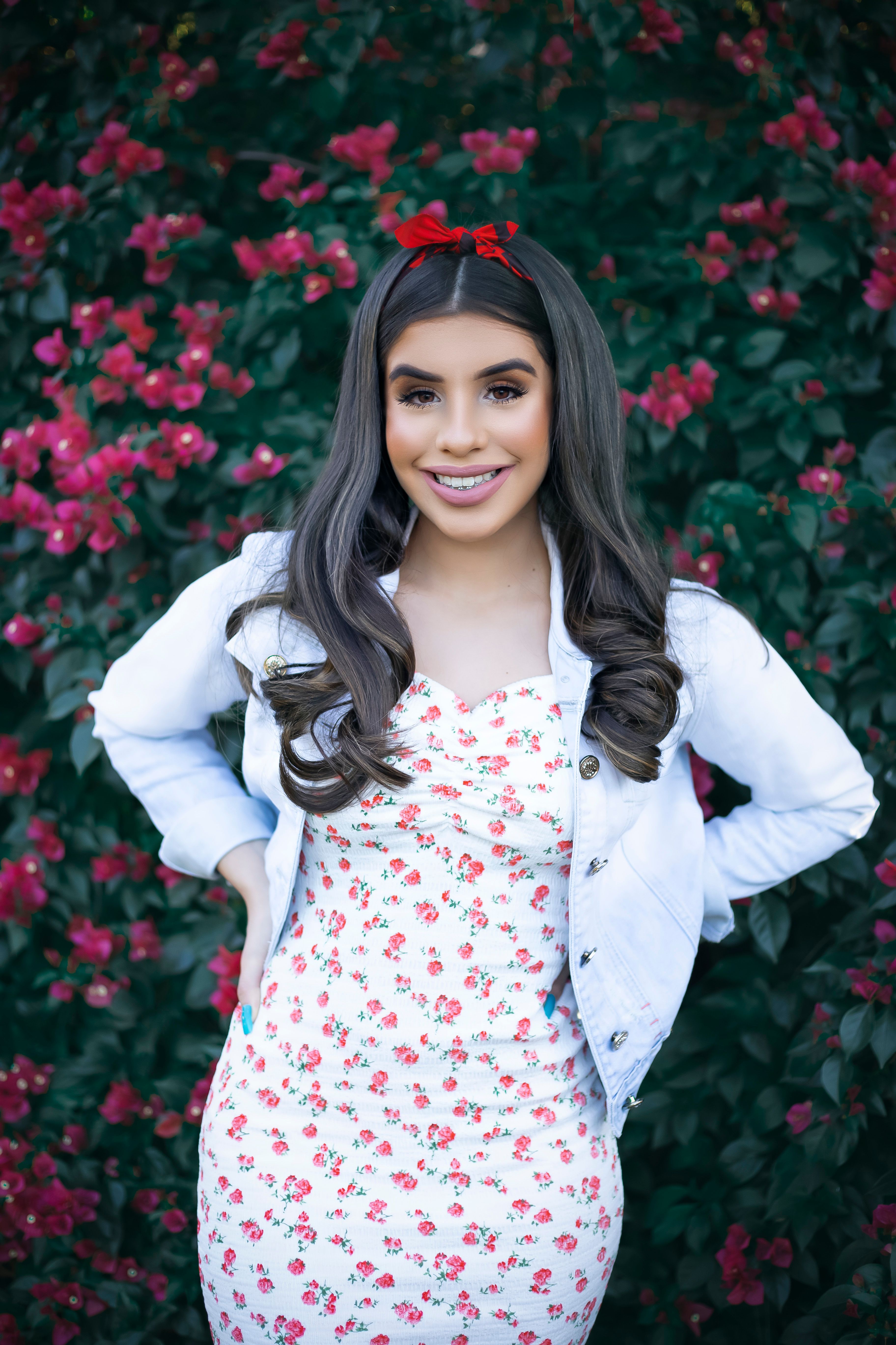 Stylish woman in white jacket posing against vibrant floral backdrop.