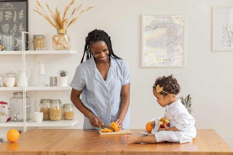 Photo Of A Woman Slicing An Orange With Her Daughter Sitting On The Tabletop