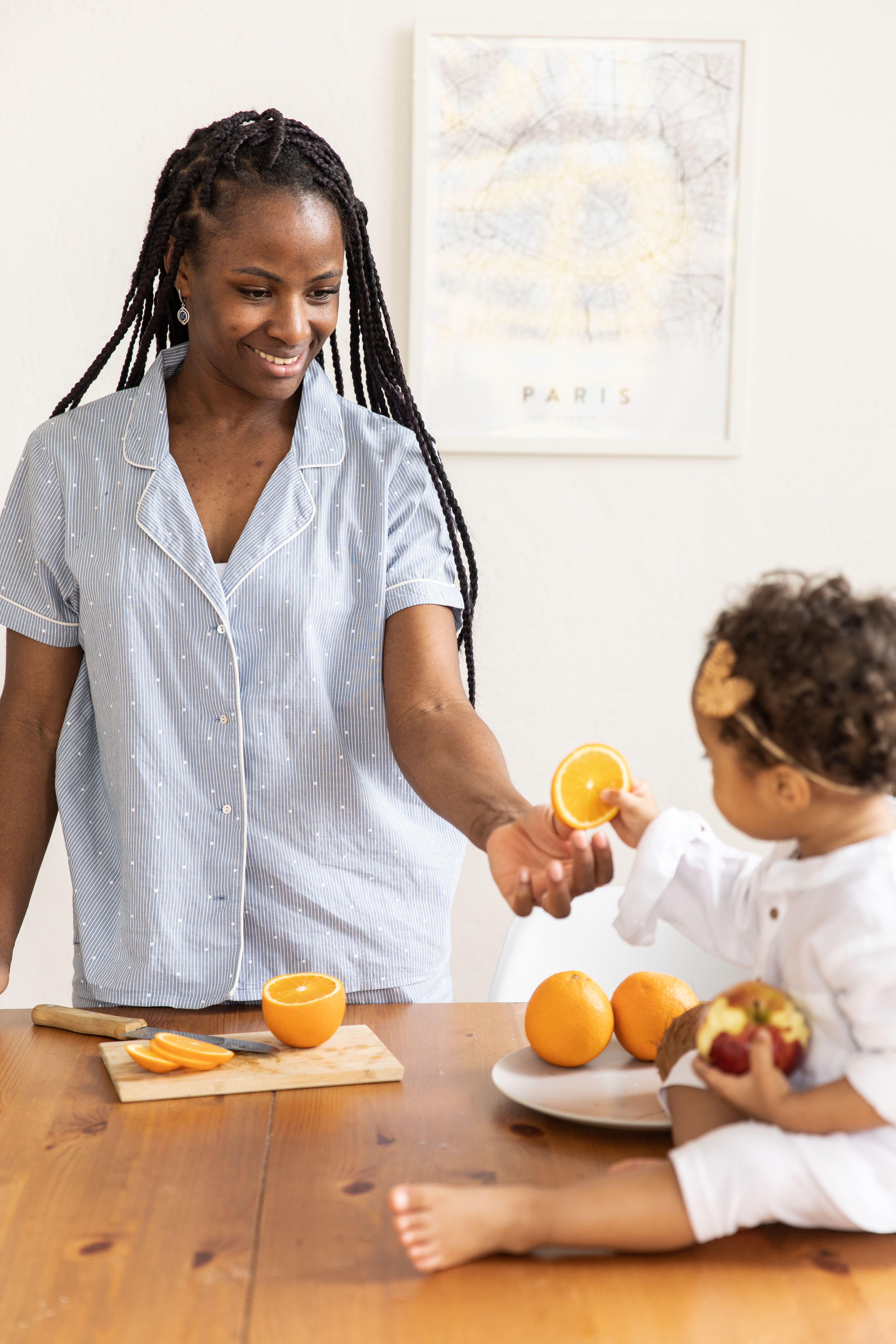 A joyful moment of a mother sharing oranges with her toddler at a table.